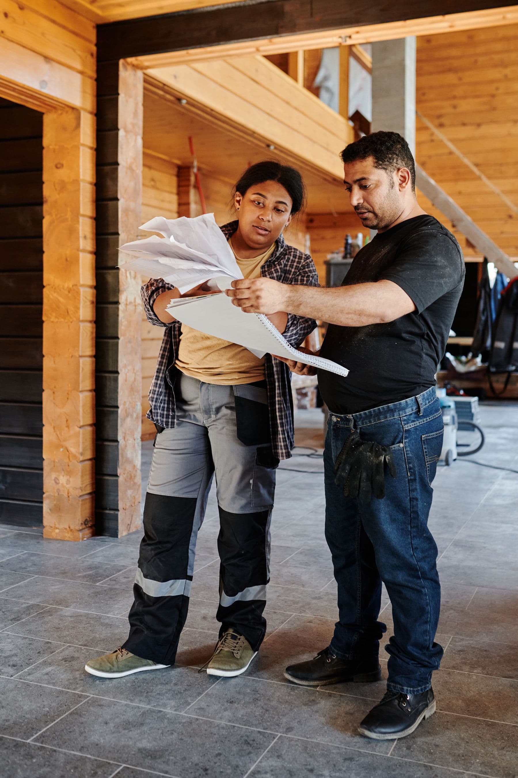 Two residential construction professionals reviewing plans inside a wooden home